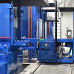 Blue Bodycote machine with logo, metallic and blue-painted equipment, and control panel among large metal structures in a factory.