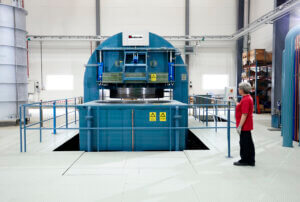 Person in red shirt beside large blue HIP vessel with safety railings in tidy facility; shelves and equipment visible behind.