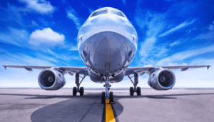Front view of a commercial aeroplane on an airport runway, showing the nose, landing gear, and HVOF-coated engines under blue sky.