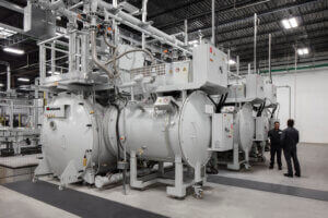 Two people stand beside large vacuum furnaces and visible control panels in Bodycote’s clean, well-lit New Fairfield facility.