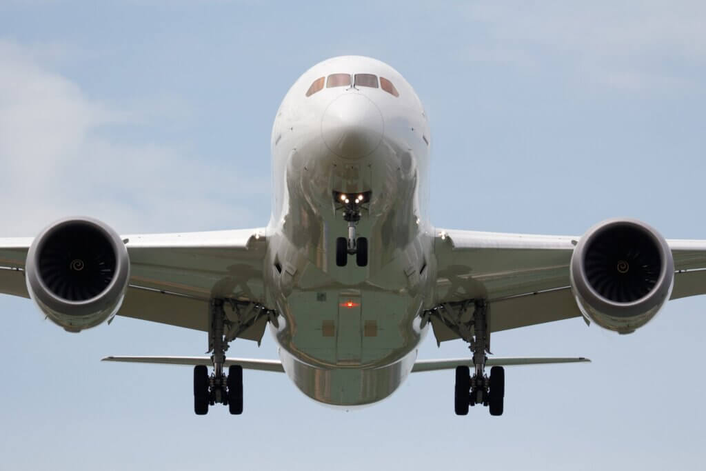 Front view of a large commercial aeroplane approaching to land with landing gear deployed and both engines visible against a clear sky.